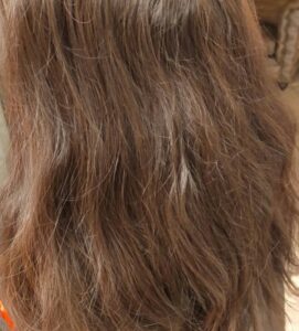 縮毛矯正の施術前。うねりと広がりのあるブラウンのロングヘアの背面
